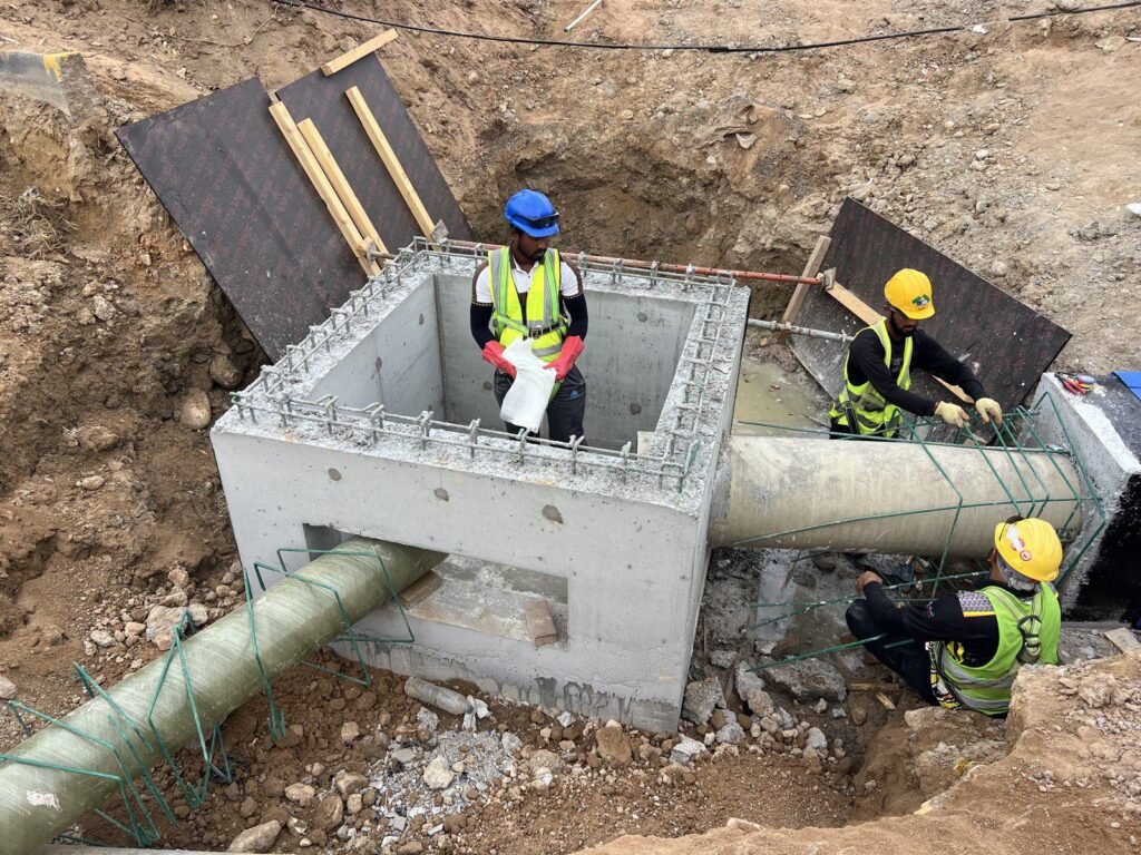 Three workers building a concrete chamber around a buried main